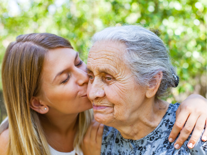 A granddaughter leans in to kiss her grandmother on the cheek while the older woman smiles