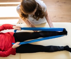Seen from above, a therapist helps a client on a mat work with a blue resistance band