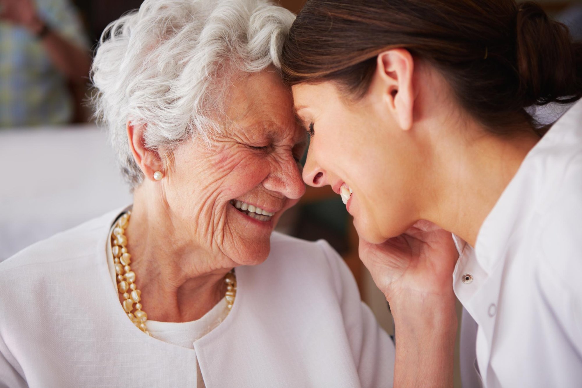 An older woman and a younger woman touch foreheads, both laughing