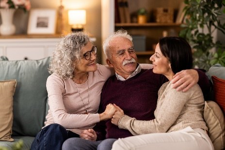 An older man on a sofa with his arms around his wife and adult daughter