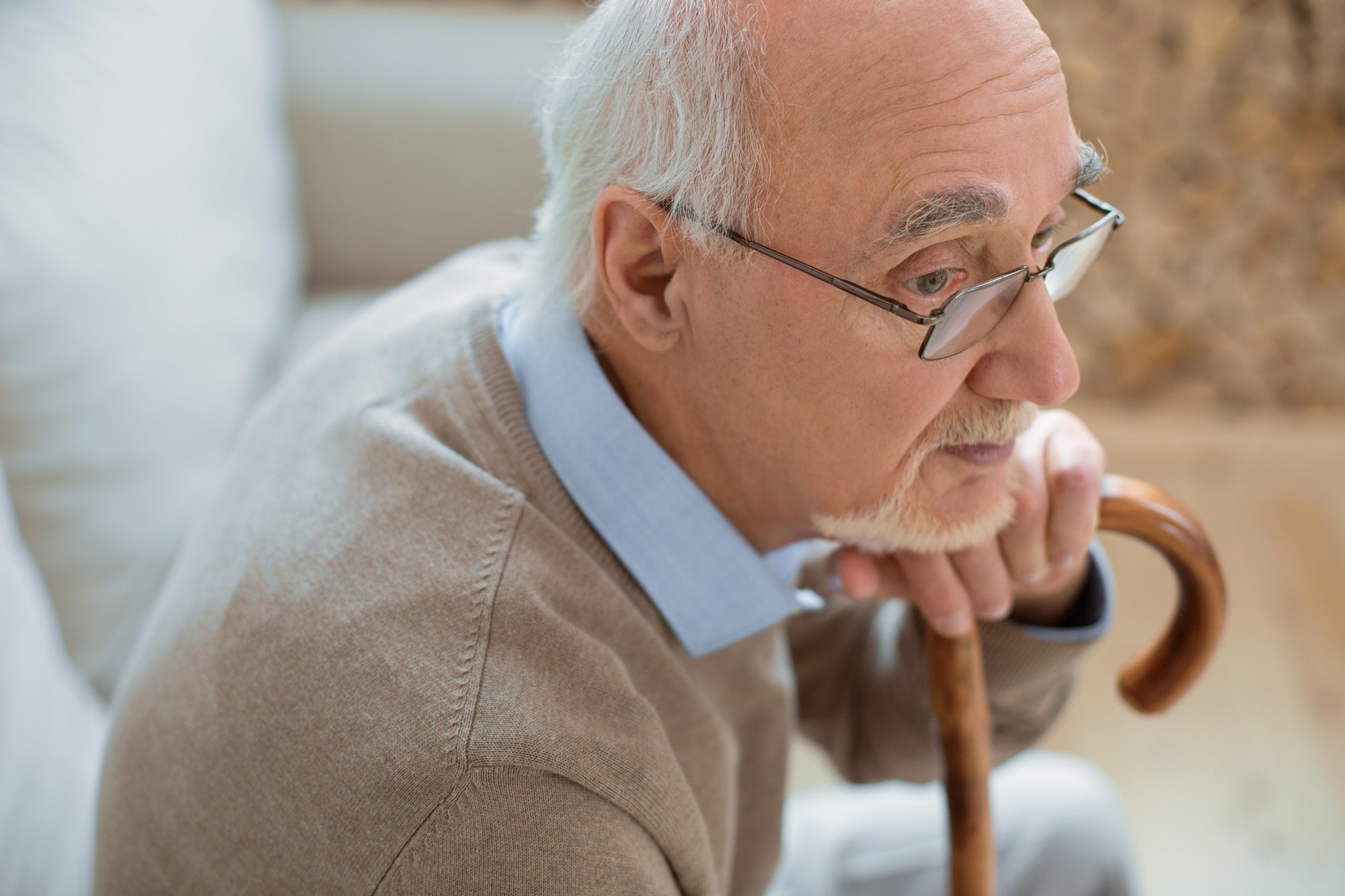 An older man rests his chin on his cane, gazing thoughtfully