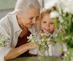 An older woman and a young child look at a vase of wildflowers together