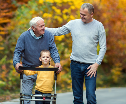 Three generations walk an autumn path, the grandfather steadying himself on a walker